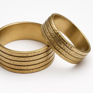 May include: Two gold-colored, hammered metal rings. The larger ring is on the left, with the smaller ring leaning against it on the right. Both rings have a textured surface with horizontal lines.