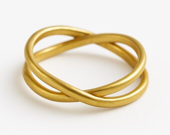 May include: A gold ring featuring a smooth, matte finish and a crossover design. The band consists of two thin, rounded metal strands that intersect at two points, creating an open, continuous loop structure with a soft, warm yellow tone.
