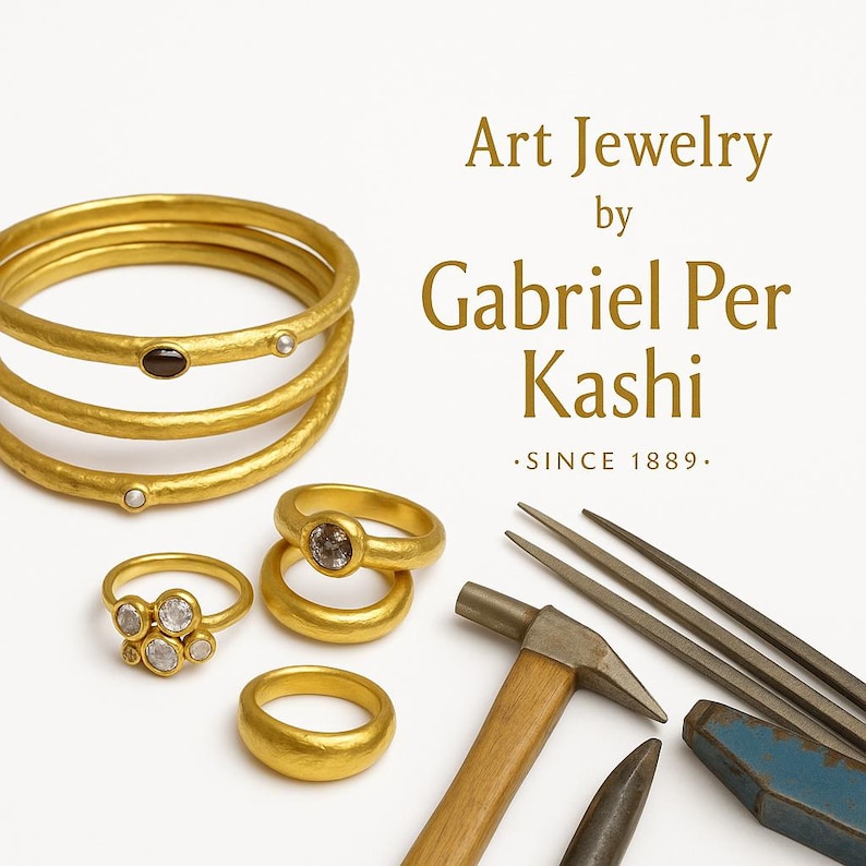 May include: Gold jewelry set against a white background. The image features multiple rings, including a stack of three gold bangles, and rings with gemstones. The text reads "Art Jewelry by Gabriel Per Kashi .SINCE 1889."
