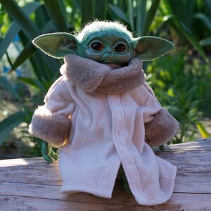 May include: A green plush toy with large ears and brown eyes wearing a white coat with a brown fur collar and cuffs. The toy is sitting on a wooden log.