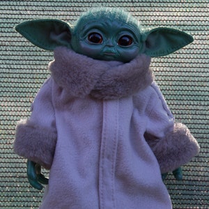 May include: A plush toy of a green alien character wearing a white coat with a fur collar and cuffs. The character has large ears and big brown eyes.