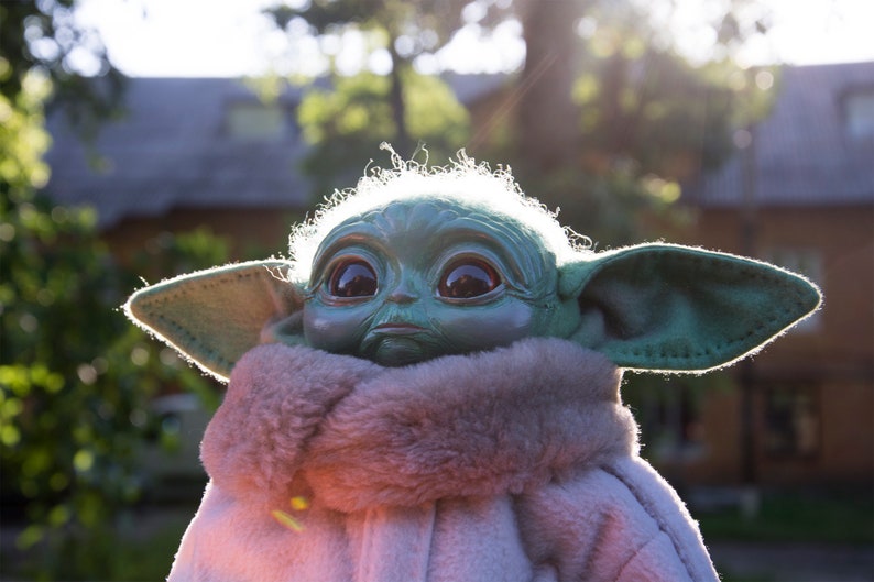 May include: A green plush toy with large eyes and a furry white collar. The toy is wearing a white coat and has large ears.