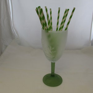May include: A green glass goblet with a frosted design filled with green and white striped paper straws.