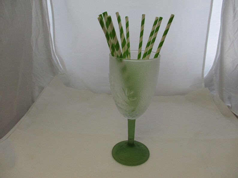 May include: A green glass goblet with a frosted design filled with green and white striped paper straws.