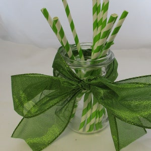 May include: A glass jar with a green ribbon tied around it. The jar is filled with green and white striped paper straws.