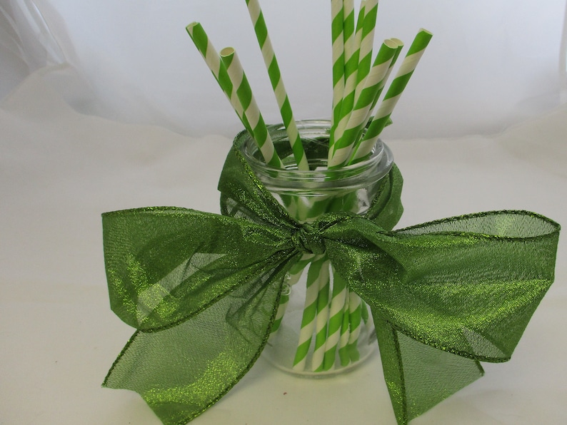 May include: A glass jar with a green ribbon tied around it. The jar is filled with green and white striped paper straws.