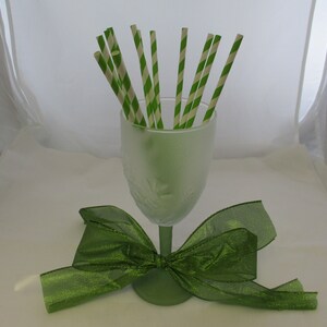 May include: A frosted green glass vase filled with green and white striped paper straws, with a green satin bow tied around the base.