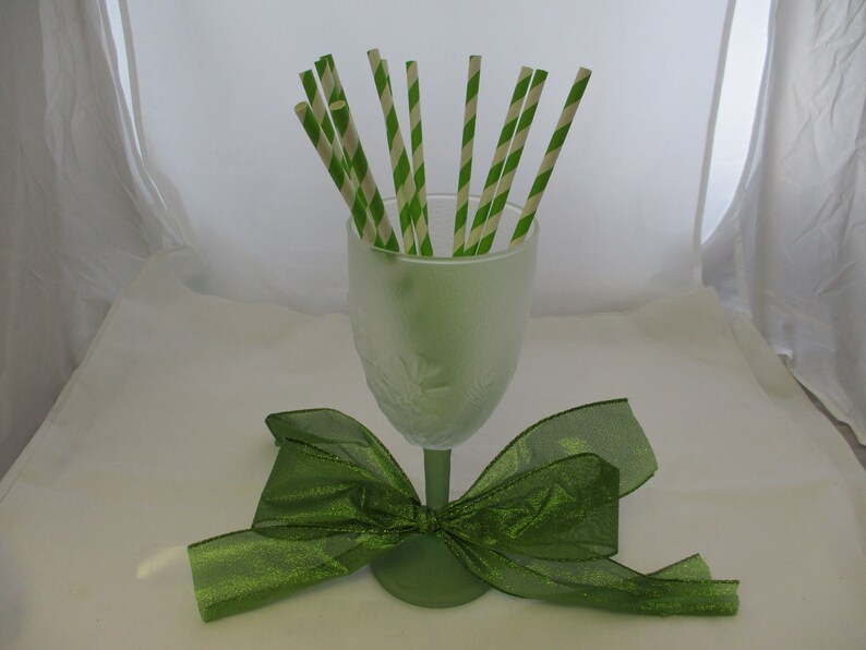 May include: A frosted green glass vase filled with green and white striped paper straws, with a green satin bow tied around the base.