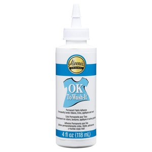 May include: A white bottle of Aleene's Original OK To Wash-It permanent fabric adhesive. The bottle has a blue band and a blue graphic of a shirt. The bottle contains 4 fl oz (118 mL) of adhesive.