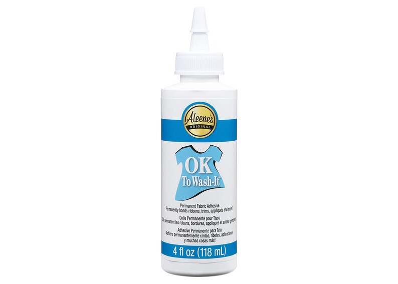 May include: A white bottle of Aleene's Original OK To Wash-It permanent fabric adhesive. The bottle has a blue band and a blue graphic of a shirt. The bottle contains 4 fl oz (118 mL) of adhesive.
