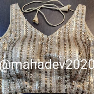 Puede incluir: Top beige con lentejuelas, escote en V y filas verticales de lentejuelas. El top tiene un cierre de cordón y el texto "@mahadev2020" es visible.