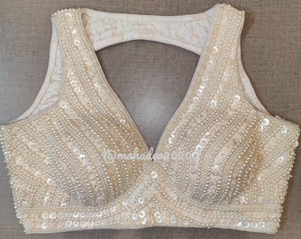 May include: A white sleeveless blouse with a deep V-neckline and a keyhole back. The blouse is embellished with pearl-like sequins and beads.