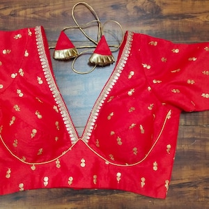 Pu&ograve; includere: Una blusa rossa ricamata con bordi dorati e una profonda scollatura a V. La blusa ha maniche corte e un corpetto aderente.