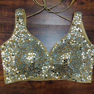 May include: A gold-coloured, halter-style, halter top with a V-neckline, covered in small, round, silver-coloured sequins.