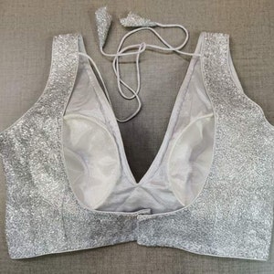 May include: A silver sequined  halter-style top with a deep V-neckline. The top is made of a sheer fabric with a lining.