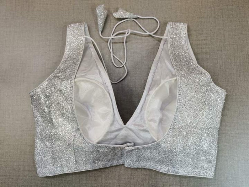 May include: A silver sequined  halter-style top with a deep V-neckline. The top is made of a sheer fabric with a lining.