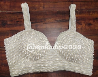 May include: A white crop top with a sweetheart neckline, completely covered in white pearls. The top has two thin straps.