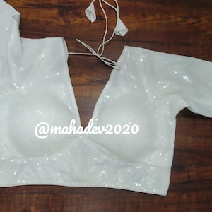 May include: White sequined blouse with a V-neck and short sleeves. The blouse has a tie at the neck and the text "@mahadev2020" is printed on the front.