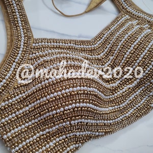 Pu&ograve; includere: Una blusa dorata e bianca con perline e un motivo ondulato. La blusa &egrave; decorata con piccole perle e perline dorate.
