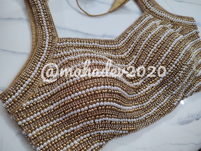 Pu&ograve; includere: Una blusa dorata e bianca con perline e un motivo ondulato. La blusa &egrave; decorata con piccole perle e perline dorate.