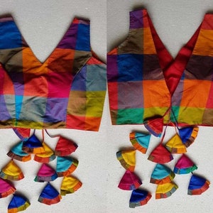 May include: A colorful checkered sleeveless blouse with a V-neckline and a tie closure. The blouse has a multi-colored checkered pattern with tassels at the bottom.