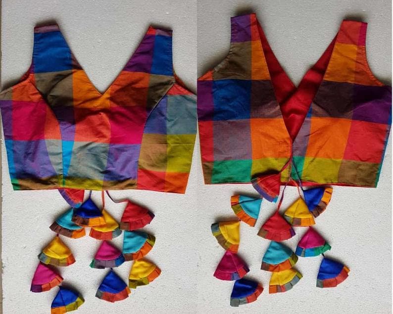 K&ouml;nnte beinhalten: Eine bunte, &auml;rmellose Bluse mit Karomuster, V-Ausschnitt und Bindeverschluss. Die Bluse hat ein mehrfarbiges Karomuster mit Quasten am Saum.