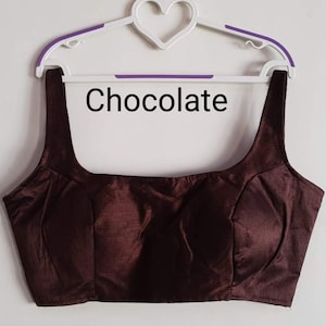 May include: A brown sleeveless blouse with a scoop neck. The blouse is on a hanger and the word "Chocolate" is written on a white background behind the blouse.