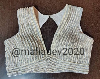 May include: A white beaded blouse with a deep V-neckline. The blouse is decorated with rows of pearls and has a  "@mahadev2020" watermark.