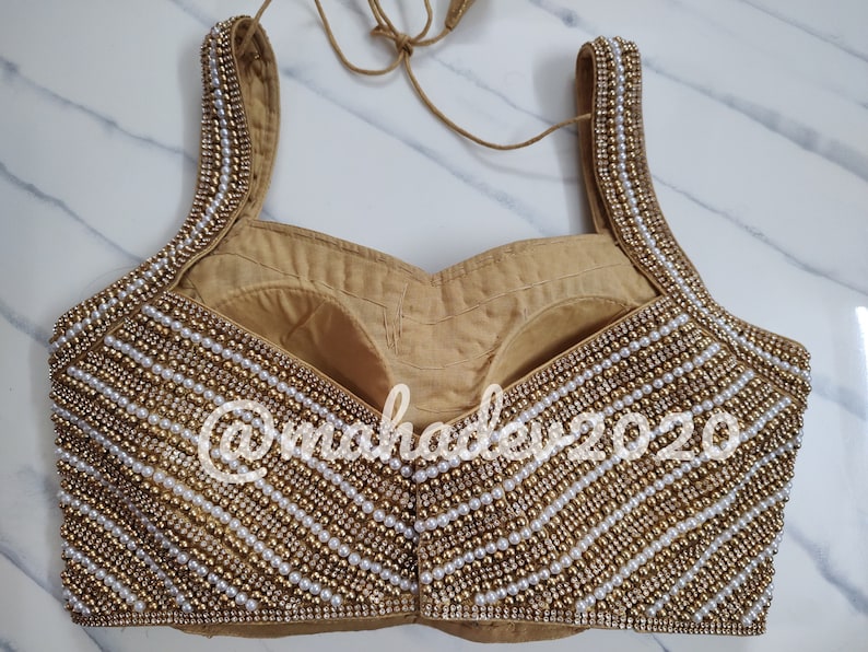 Pu&ograve; includere: Un choli dorato e bianco con perline e scollatura a cuore. Il choli &egrave; decorato con file di perle e perline dorate.