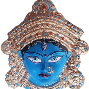 May include: A blue and gold Hindu deity mask with intricate details. The mask features a third eye and a nose ring. The deity is adorned with a crown and a necklace.