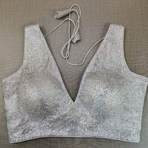 May include: A silver sequined sleeveless blouse with a deep V-neckline.