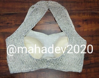 May include: A white halter top with a low back, embellished with silver and white beads. The top has a triangular neckline and is fully beaded.