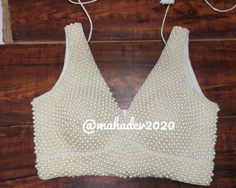 May include: A white sleeveless blouse with a deep V-neckline, completely covered in white pearls. The blouse has a simple design and is adorned with a delicate pearl embellishment. The text "@mahadev2020" is visible on the front of the blouse.