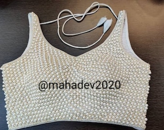 May include: A white sleeveless blouse with a scoop neck, fully covered in white pearl beads. The blouse has a thin white string tie at the neck. The text "@mahadev2020" is printed on the front of the blouse.