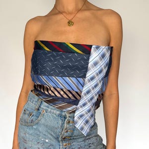 May include: A strapless top made from assorted patterned ties in blue, red, yellow, and brown. The top is worn with light-wash denim jeans. A gold necklace is also visible.