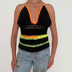 May include: A black crochet halter top with neon orange trim and accents. The top features an open weave design and is paired with light blue jeans. A stylish and colourful handmade garment.