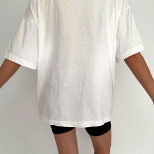 May include: An oversized white t-shirt with short sleeves. The t-shirt is made from a soft, lightweight fabric and has a relaxed fit.