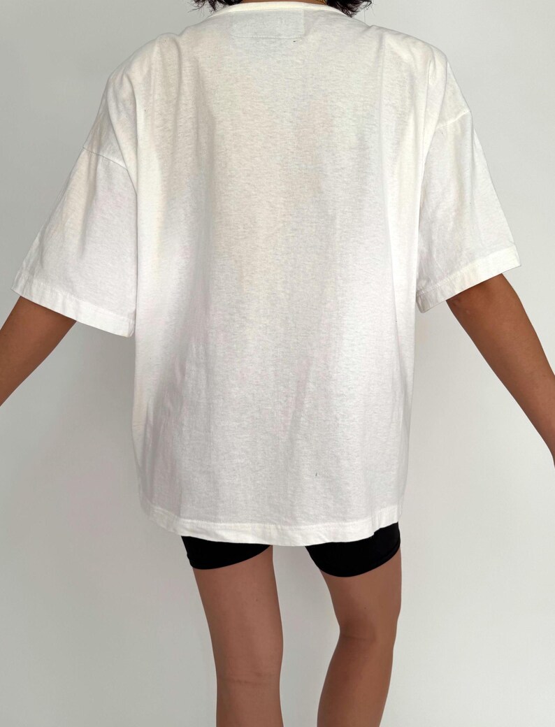 May include: An oversized white t-shirt with short sleeves. The t-shirt is made from a soft, lightweight fabric and has a relaxed fit.
