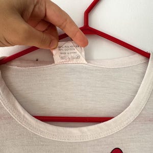 May include: White t-shirt with a red heart graphic print. The tag says "65% Polyester 35% Cotton Made in China".