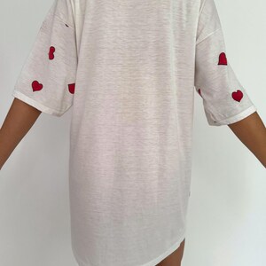 May include: White oversized t-shirt with red heart designs on the sleeves.