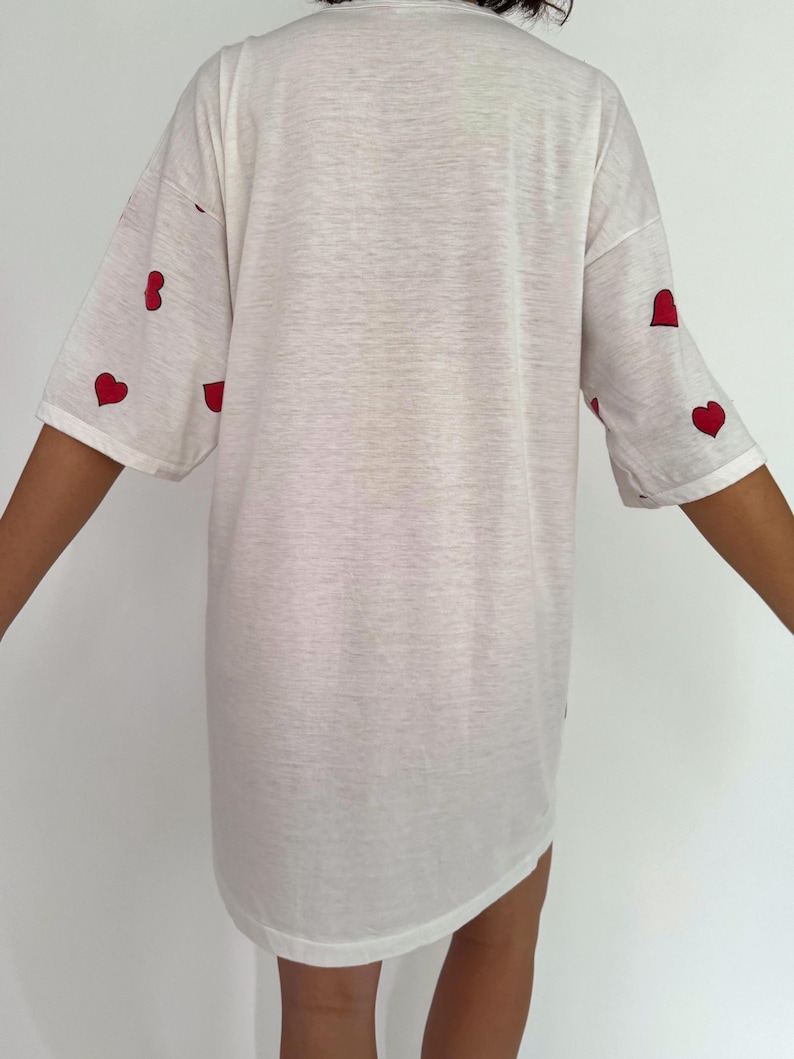 May include: White oversized t-shirt with red heart designs on the sleeves.