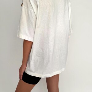 May include: An oversized white t-shirt with short sleeves and a relaxed fit. The t-shirt is worn with black cycling shorts.