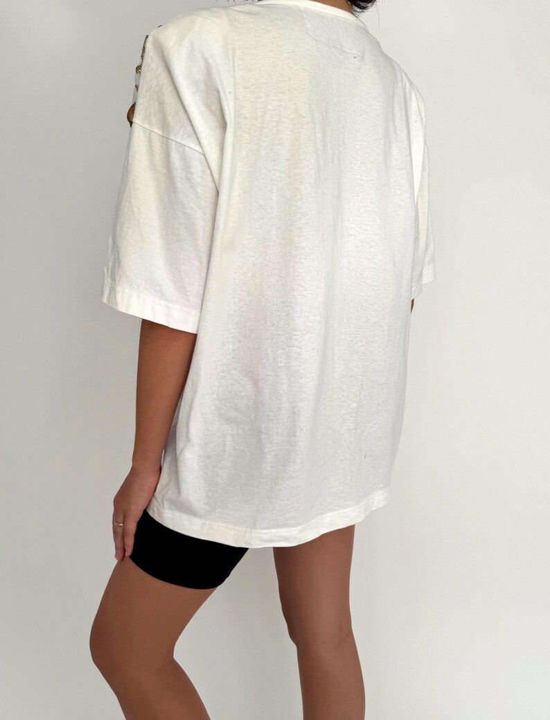 May include: An oversized white t-shirt with short sleeves and a relaxed fit. The t-shirt is worn with black cycling shorts.