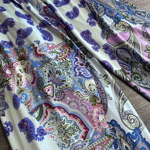 Puede incluir: Una tela blanca con un patrón de paisley en tonos de azul, rosa y verde. La tela tiene una textura suave y fluida.