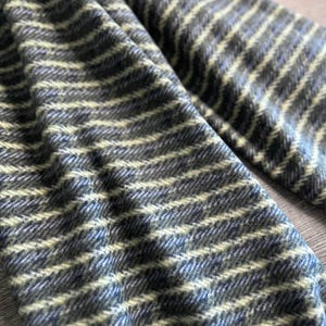 May include: A close-up of a soft, striped scarf in shades of blue and green. The scarf is made of a woven fabric with a herringbone pattern.