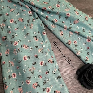 May include: A teal blue fabric with a small pink and white floral pattern. The fabric has a slightly textured surface.