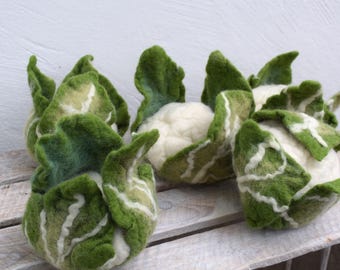 Può includere: Sculture di cavolfiori infeltriti a mano con foglie verdi e bianche. Le teste di cavolfiore sono di colore bianco crema. Le sculture sono disposte su una cassa di legno rustica, creando un'esposizione affascinante e stravagante.