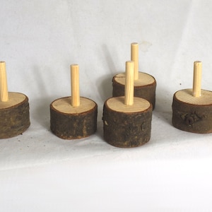 Peut inclure: Six chevilles en bois avec une finition en bois naturel sont fixées à des bases rondes en bois avec une texture d'écorce. Les bases sont disposées en demi-cercle sur une surface blanche.