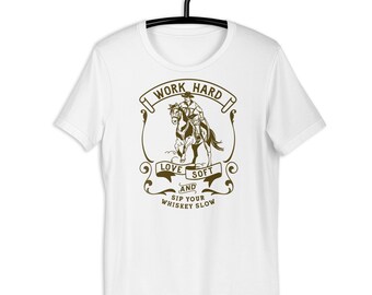 May include: White t-shirt with a brown graphic of a cowboy riding a horse. The graphic includes the text "I Work Hard Love Soft and Sip Your Whiskey Slow".