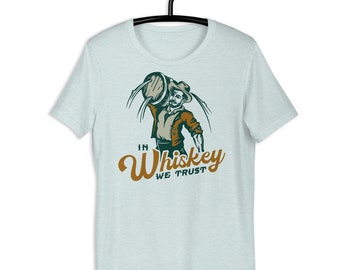 Könnte beinhalten: Ein hellblaues T-Shirt mit einer Cartoon-Illustration eines Mannes, der ein Fass Whisky hält. Der Text "In Whiskey We Trust" ist in brauner und grüner Schrift gedruckt.